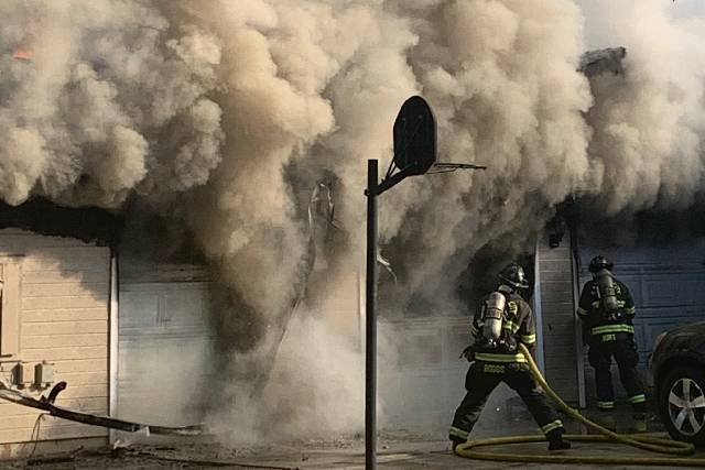 Firefighters advancing a hose line into a smoking garage